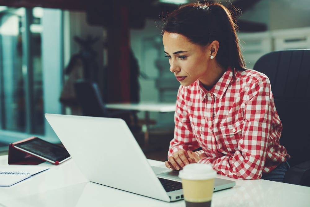 Woman in red and white plaid button down shirt researching tummy tuck with lipo options on her office computer.