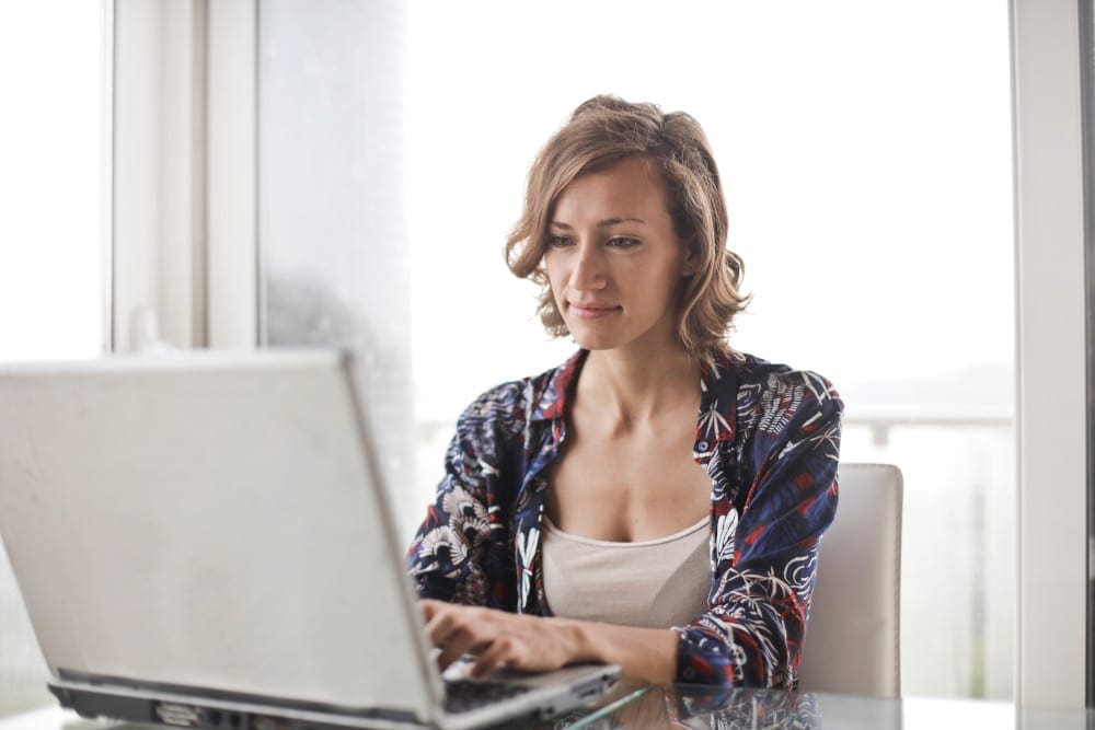 Woman in blue floral top sitting while using laptop.